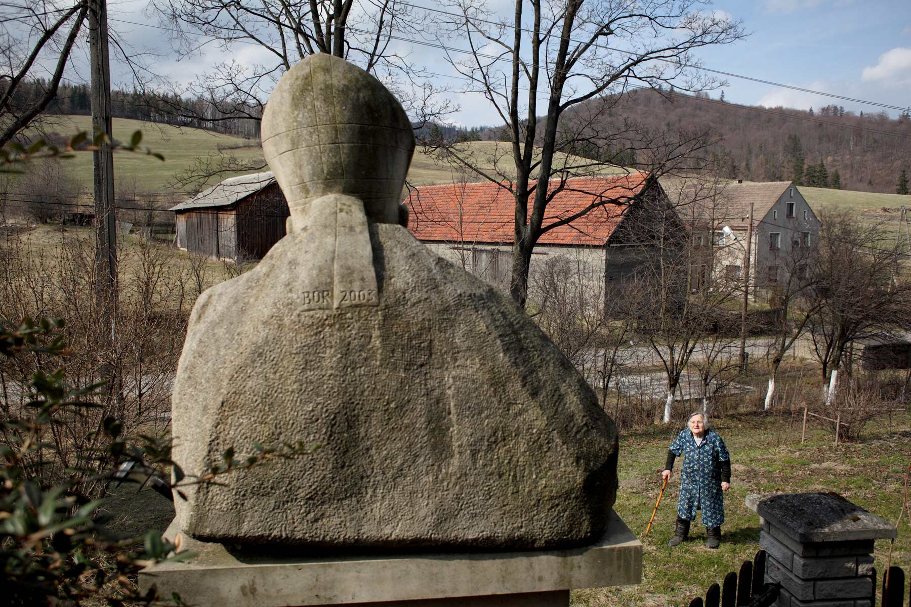 Femme âgée devant une statue du pape Jean-Paul II