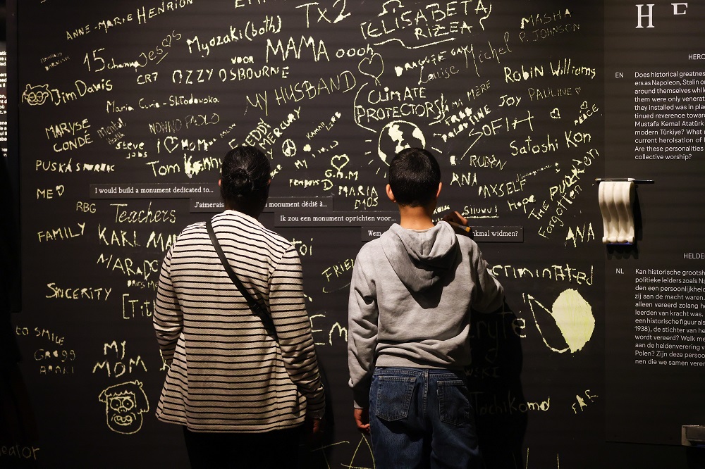 Two visitors looking at black wall with graffiti feedback