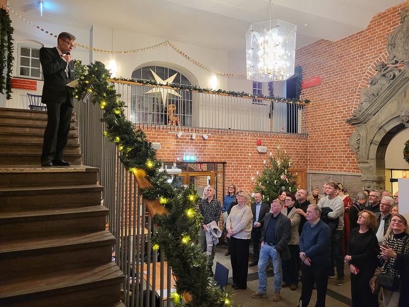 Man giving speech in museum on stairs above Christmas tree