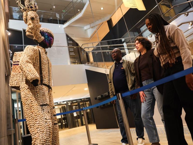 Three people looking at art model of astronaut