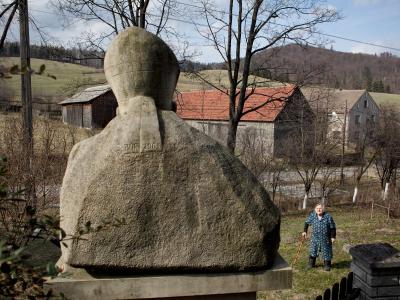 An elderly woman looks up at a statue of Pope John Paul II