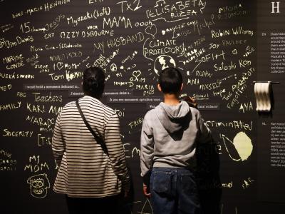 Two visitors looking at black wall with graffiti feedback