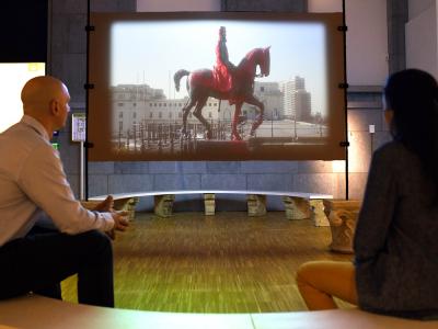 Two visitors looking at video of horse statue