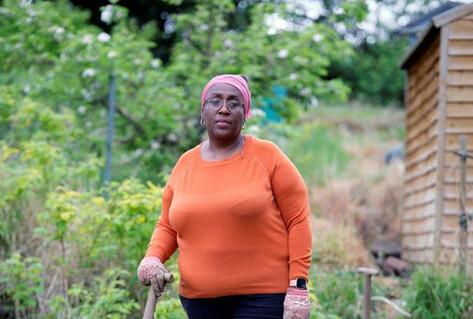 Woman standing in grass allotment with spade