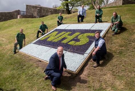 Team crouching outside by NHS flower arrangement