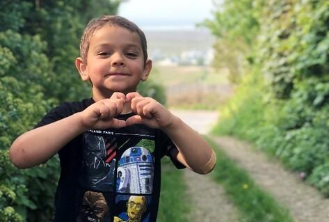 Boy making heart sign with hands outside
