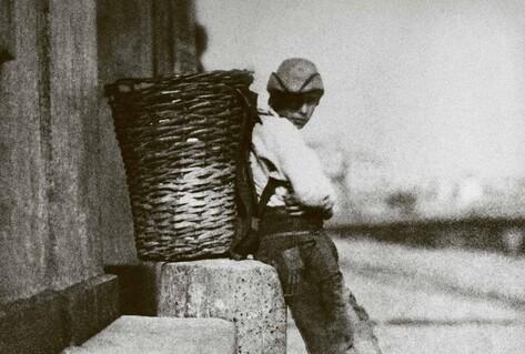 Black and white photo of boy leaning against basket